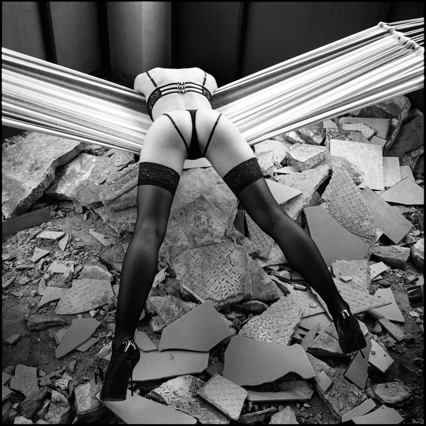 A woman in lingerie and stockings is posed over a pile of rubble.