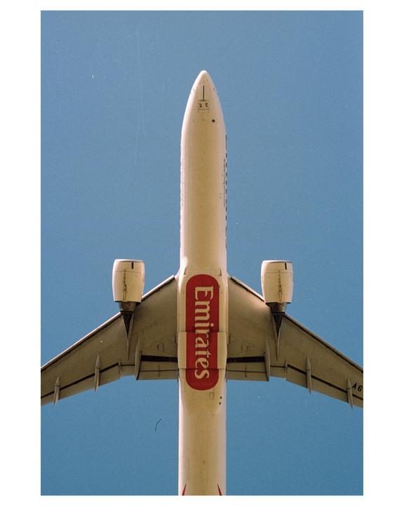 An Emirates airplane is flying overhead against a clear blue sky.