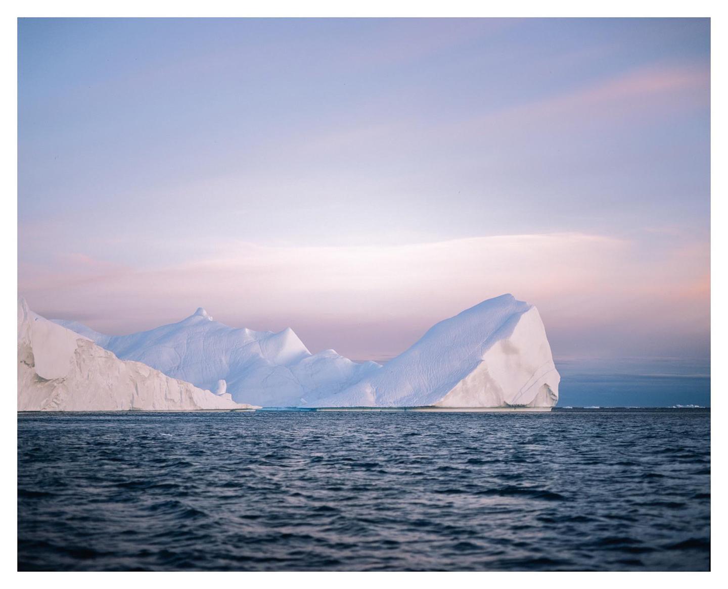 Icebergs float on the water under a pastel sky.