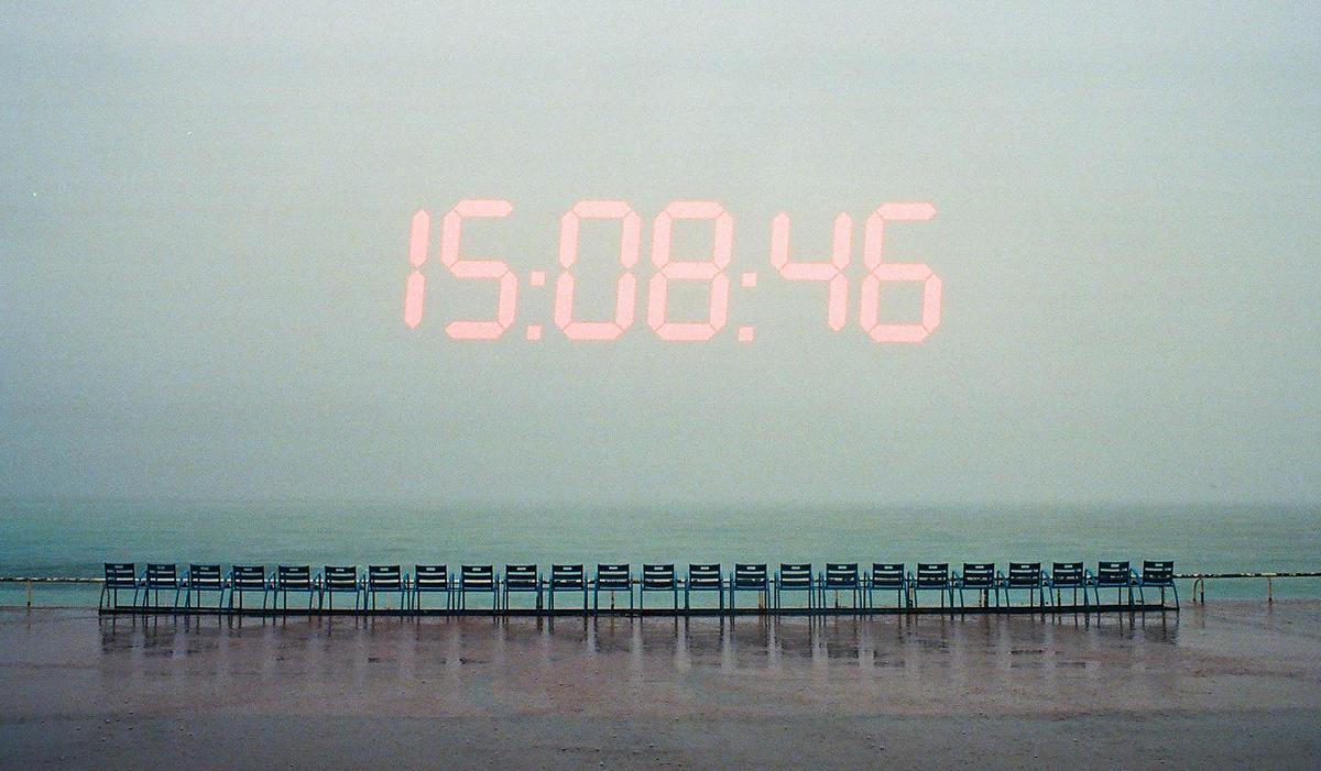 A digital clock displaying 15:08:46 is visible above a row of chairs facing the ocean.