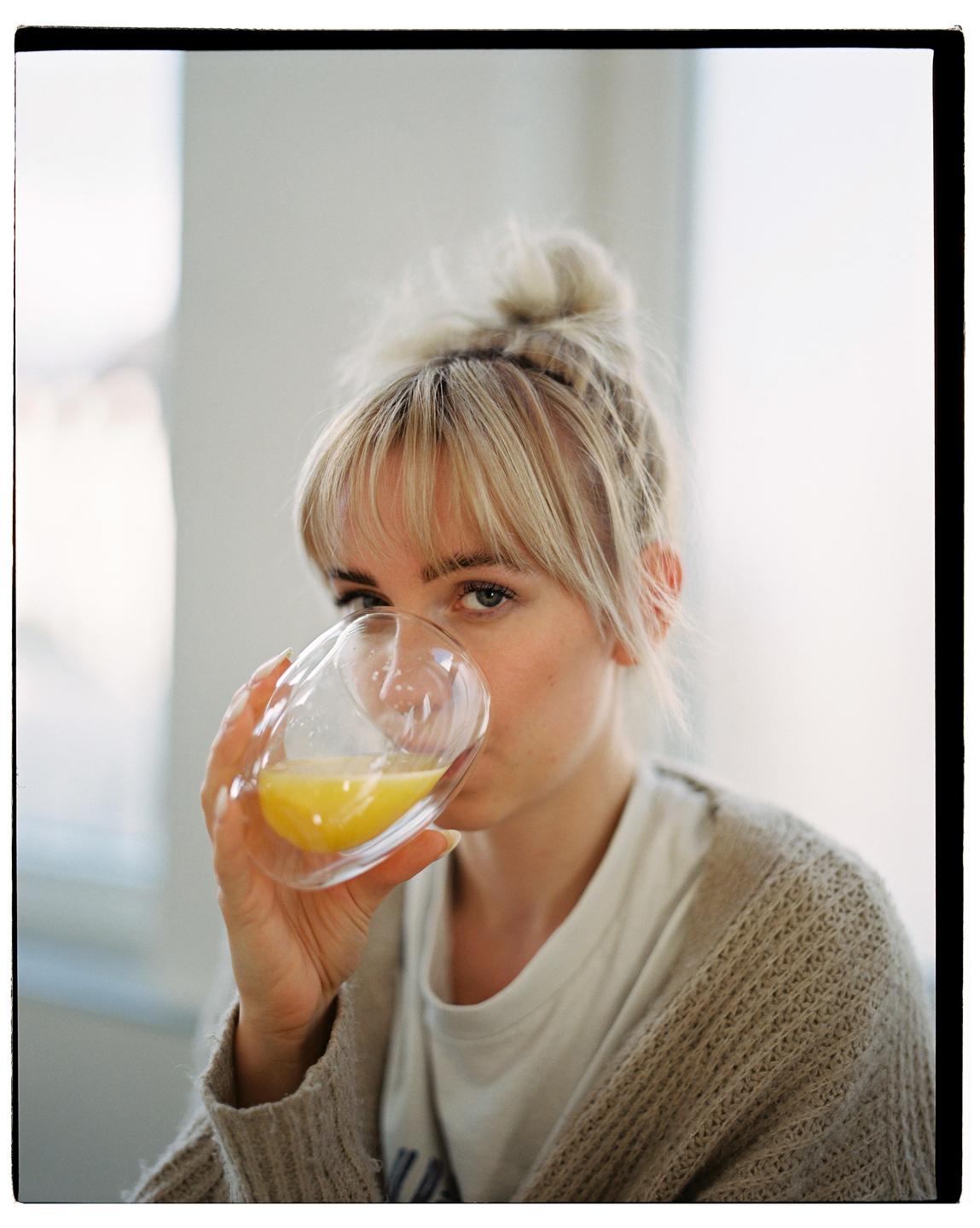 A woman with blonde hair in a bun drinks orange juice from a glass.