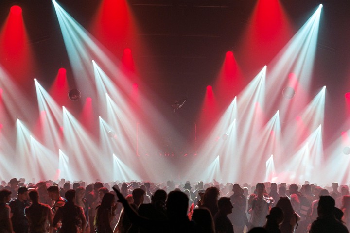 A crowd of people are silhouetted against bright red and white stage lights at a concert.