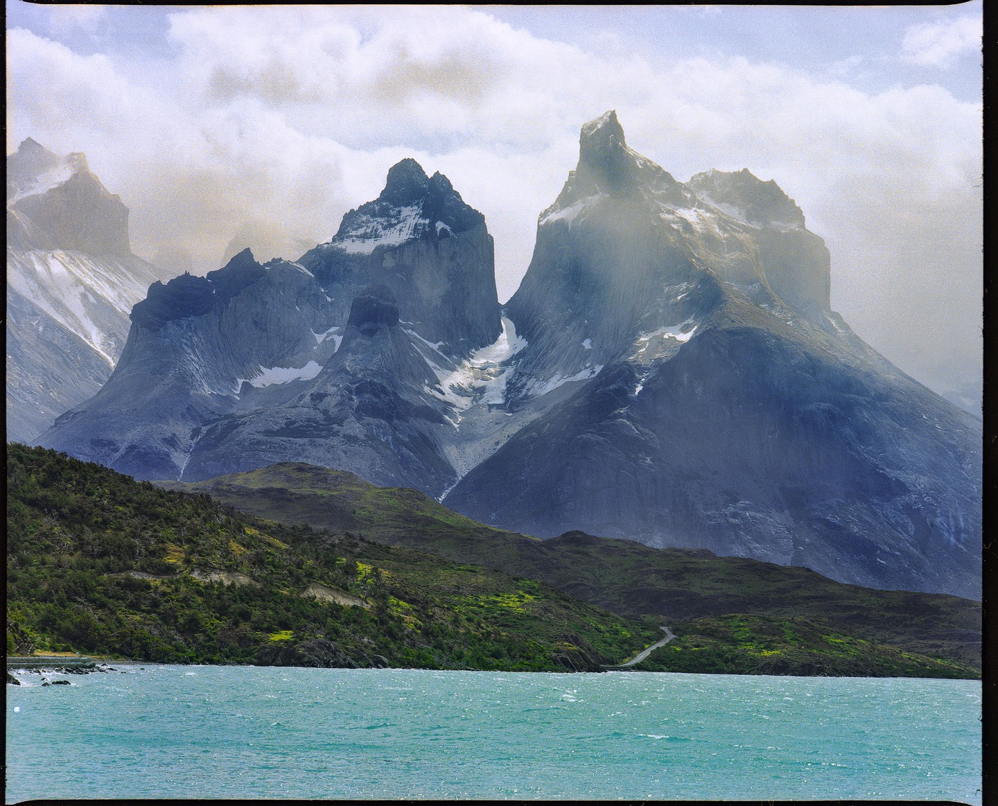 A body of water with mountains and green hills under a cloudy sky.