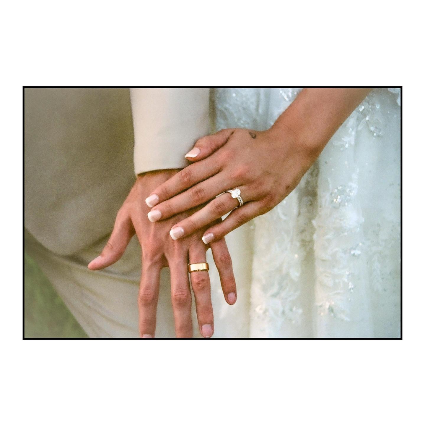 A couple's hands are clasped together, showing their wedding rings.
