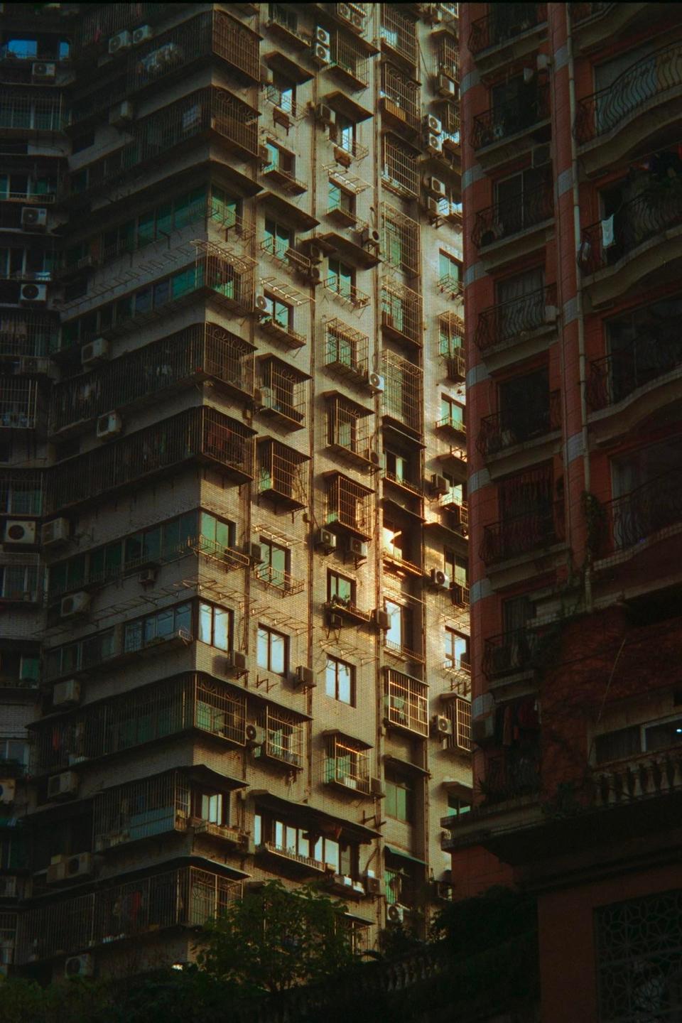 Sunlight illuminates the windows and balconies of a tall residential building in Chongqing.