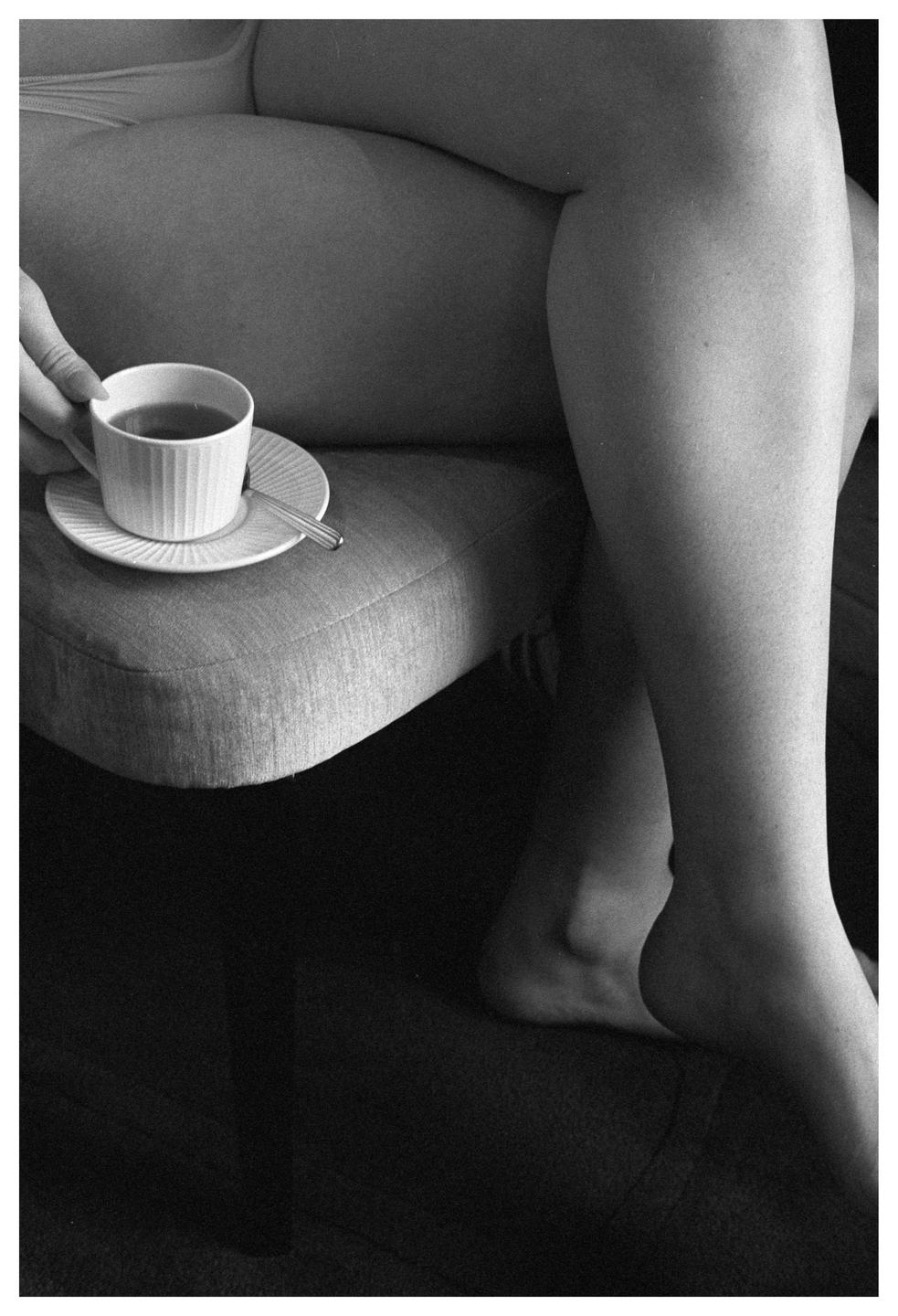 A person holds a cup of tea while sitting on a chair.