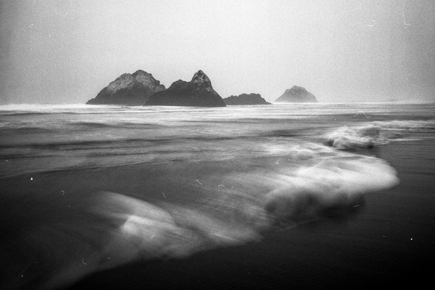 Waves crash on a beach with several rocky islands in the distance.