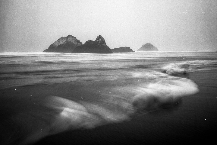 Waves crash on a beach with several rocky islands in the distance.
