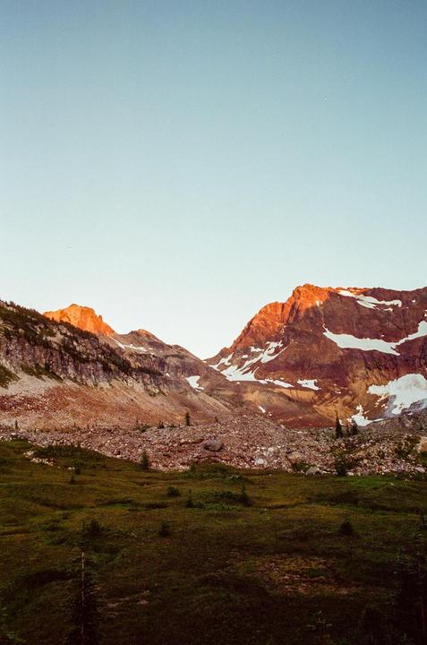 A mountain range with snow-capped peaks and a green valley is illuminated by the golden hour light.
