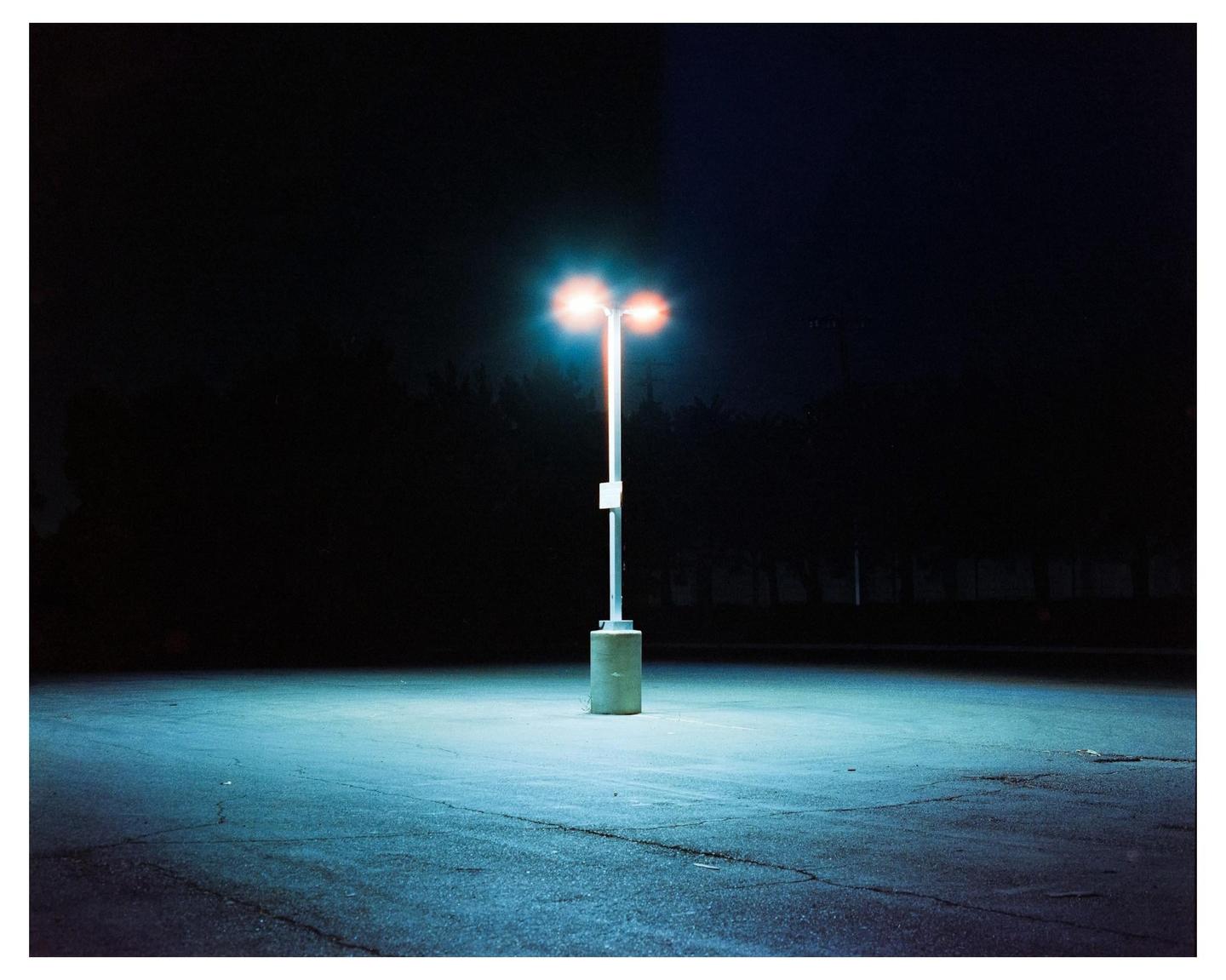 A single street light illuminates an empty parking lot at night.