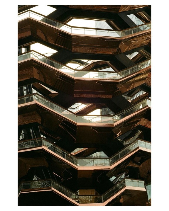 A modern building with a complex, geometric structure of interconnected staircases and platforms is shown from a low angle.