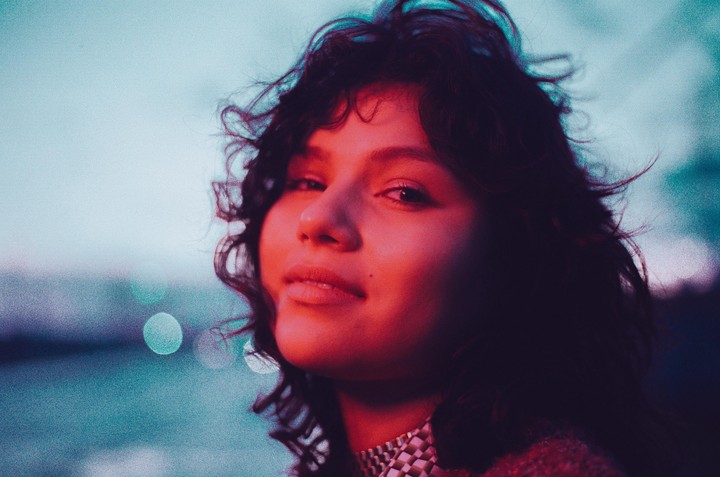 A woman with curly hair and a patterned collar looks up at the camera with a red glow on her face.