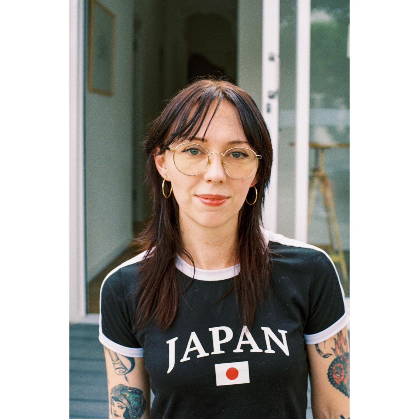 A woman with dark hair and glasses wears a black t-shirt with "JAPAN" written on it.