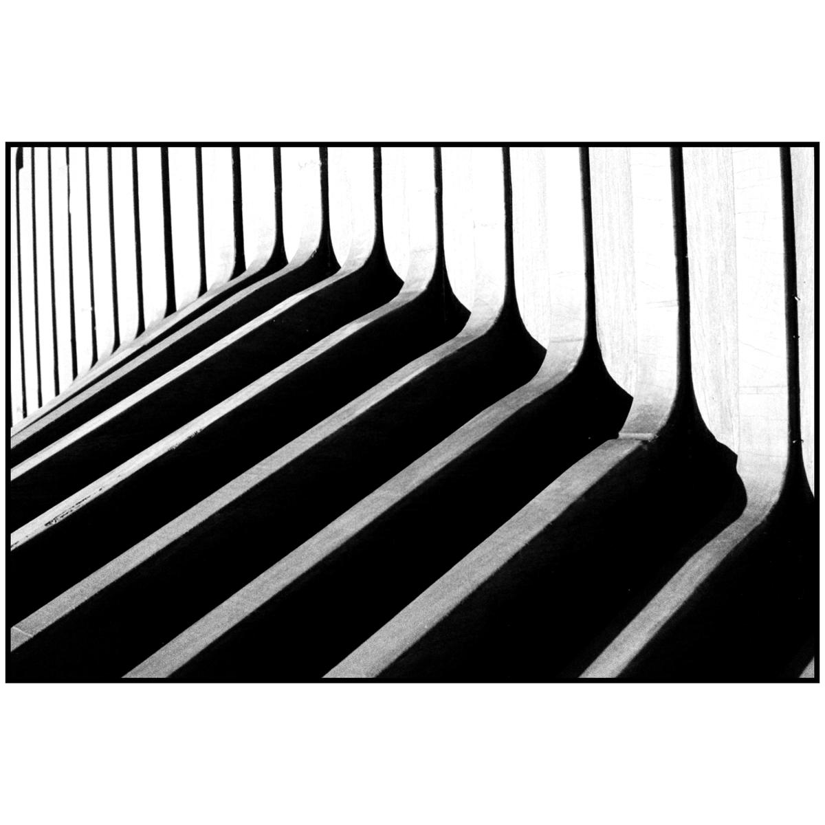 A series of vertical architectural elements cast long, diagonal shadows across a surface.