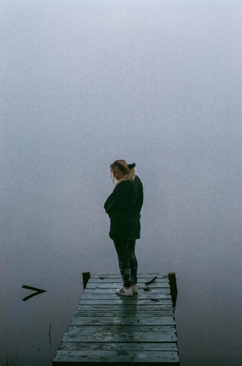 A woman stands on a wooden dock overlooking a foggy lake.