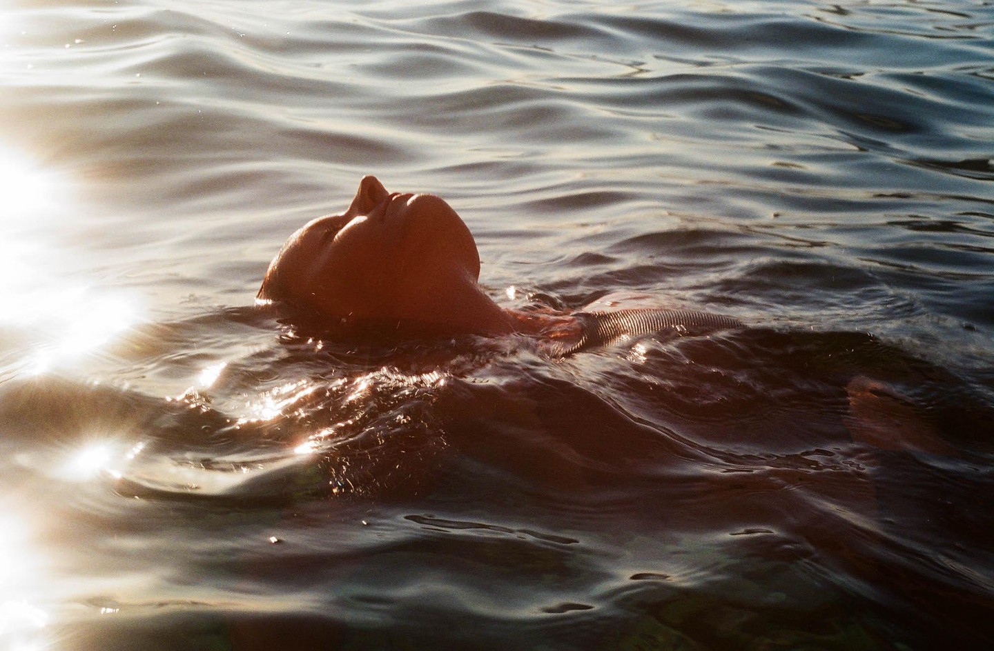 A person floats on their back in water with sunlight reflecting on the surface.
