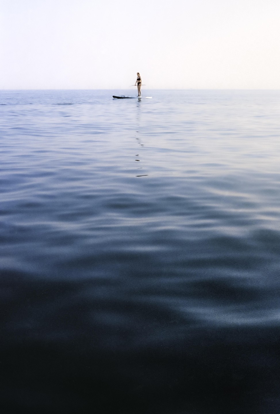 A woman stands on a paddleboard in the middle of a calm body of water.