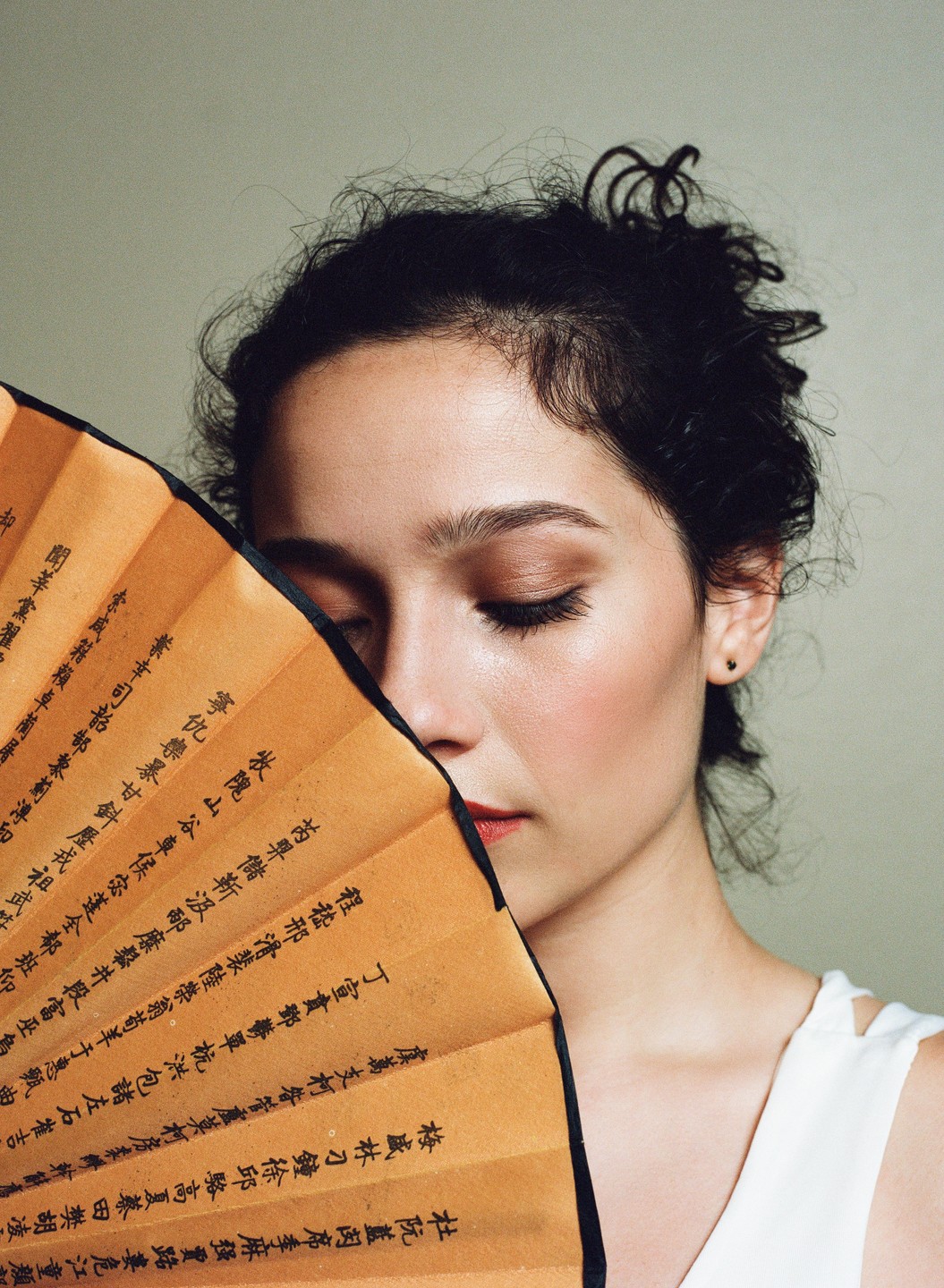 A woman with her eyes closed holds a fan with writing on it in front of her face.