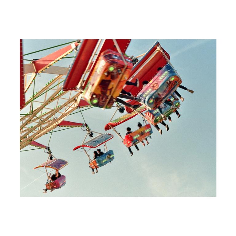 People ride a colorful swing ride at a funfair against a clear sky.