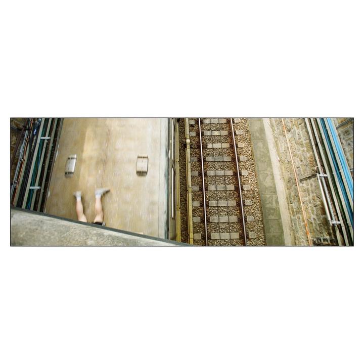 A person's legs are visible on the roof of a train next to train tracks.
