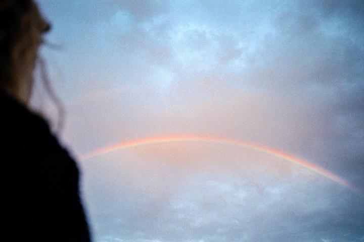 A rainbow is visible in the sky with a person's head and shoulder in the foreground.