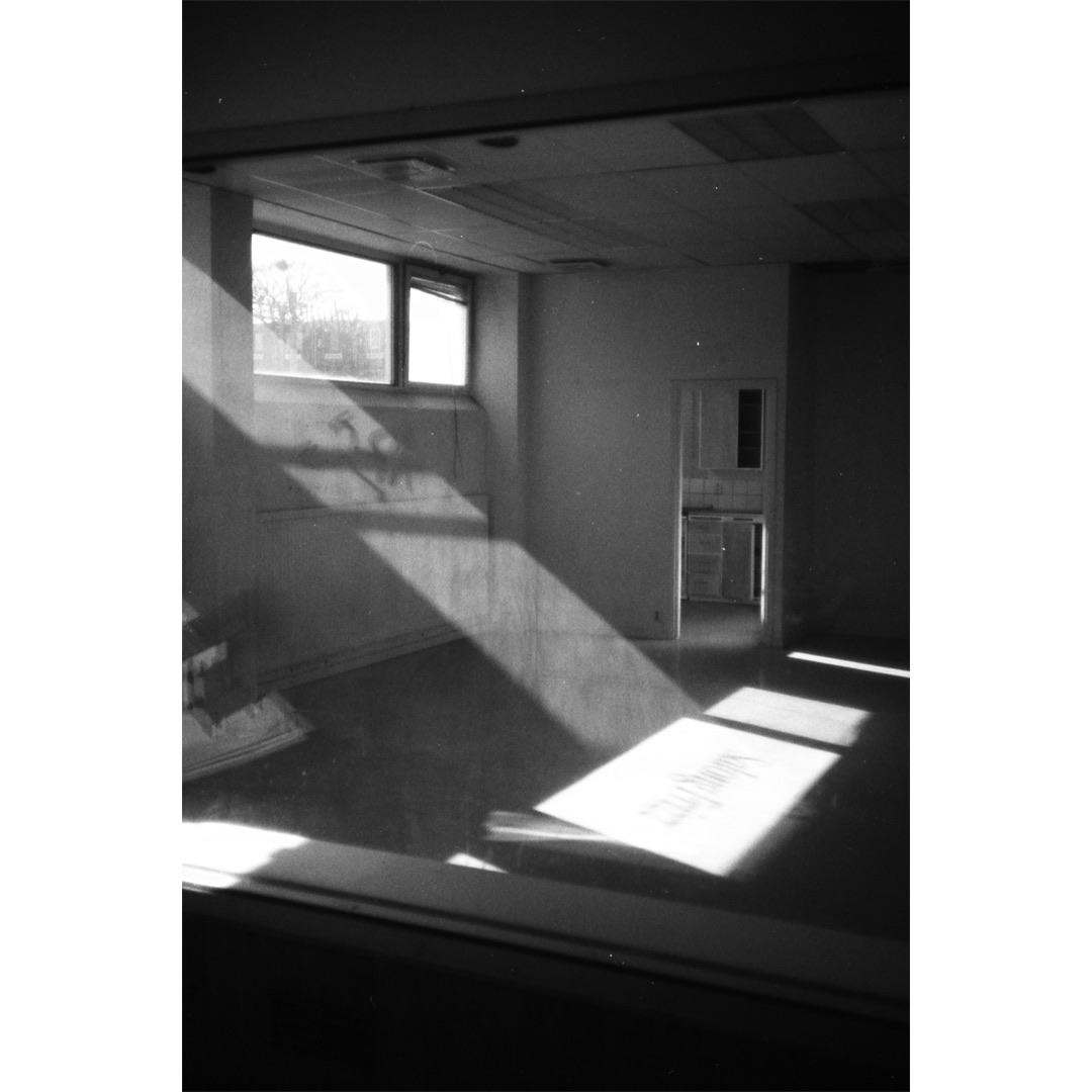 Sunlight streams through a window into an empty room with a doorway leading to another room.