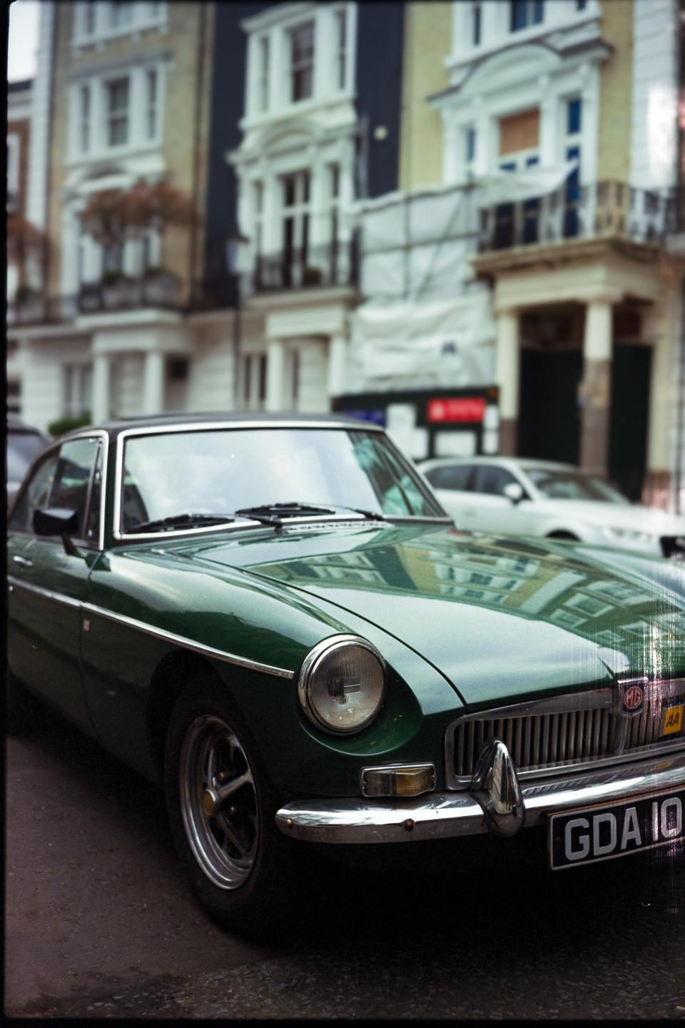 A green vintage car is parked on a street in front of buildings.