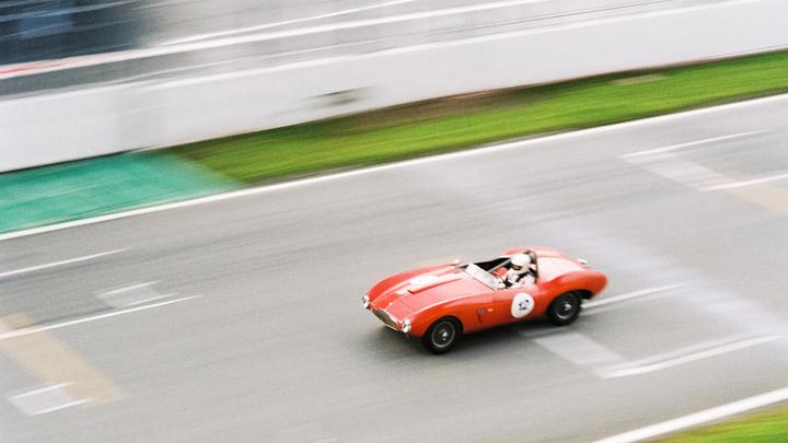 A red vintage racing car with a driver is speeding on a track.