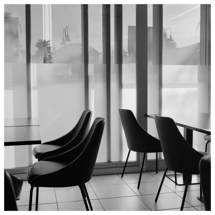 A cafe interior with chairs and tables is visible through a window with blinds.