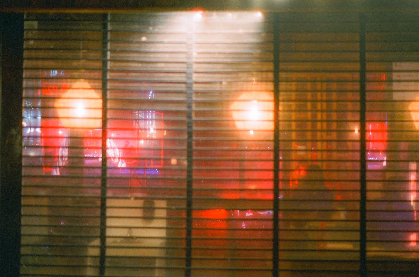 A blurry reflection of a ferris wheel is visible through window blinds at night.