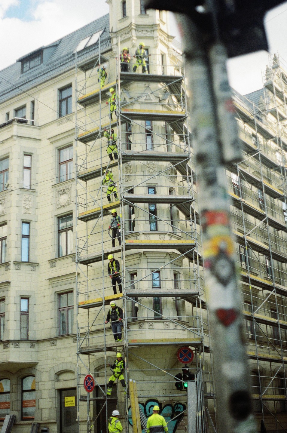 Construction workers in safety gear are climbing scaffolding on the side of a building.