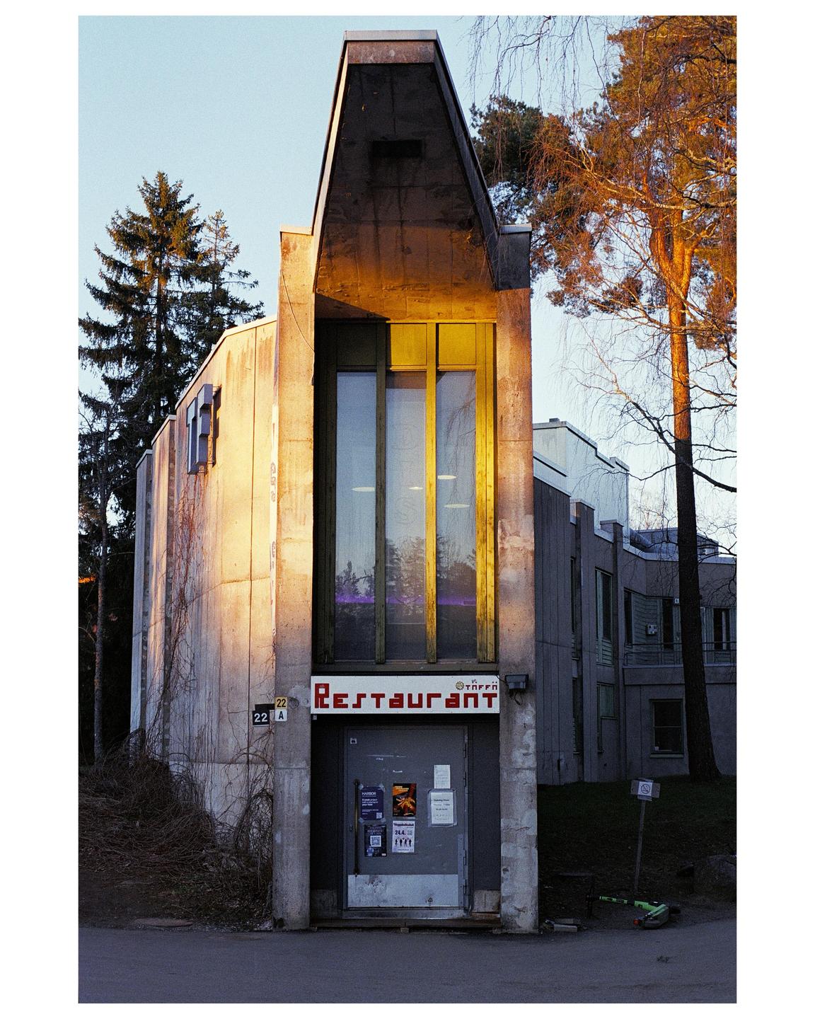 A concrete building with a red "Restaurant" sign above a door is surrounded by trees.
