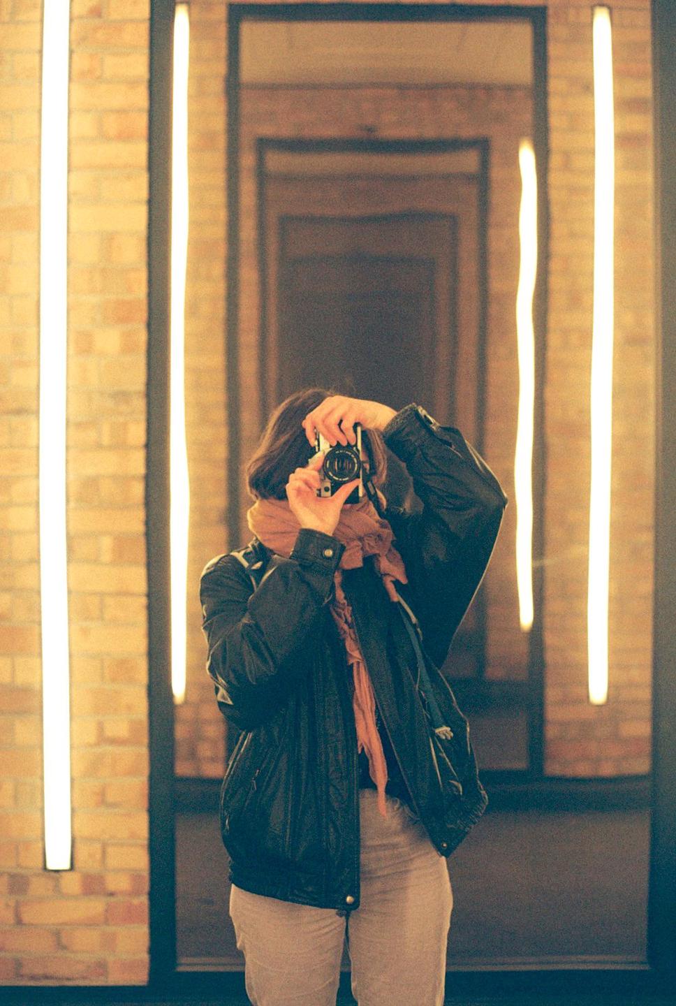 A woman takes a self-portrait in a mirror, holding a camera to her face.