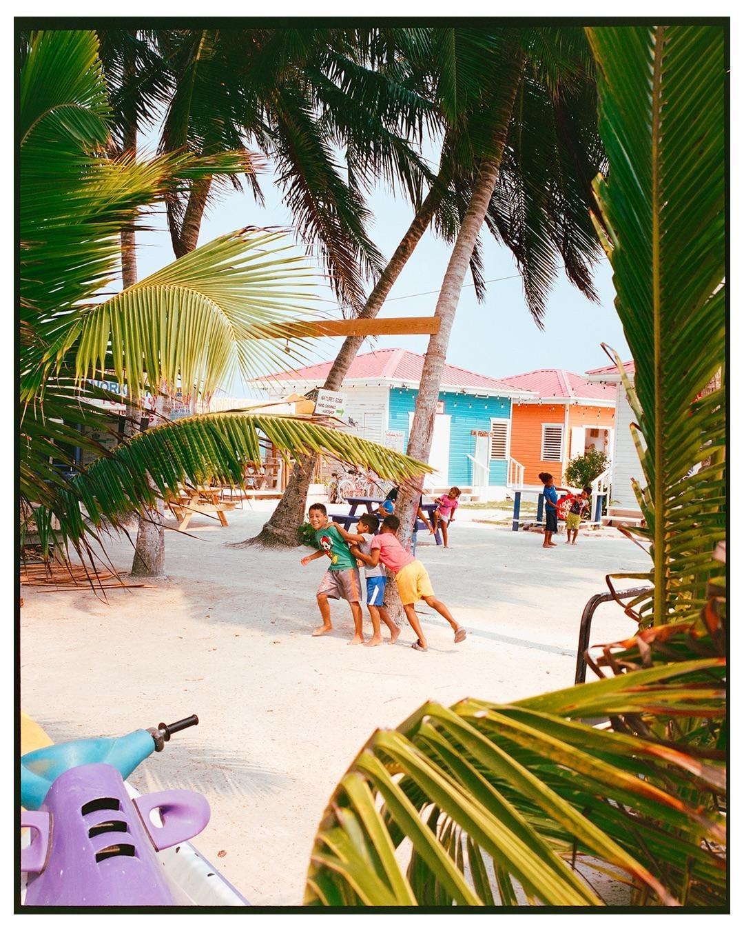 Children play on a sandy beach surrounded by palm trees and colorful buildings.