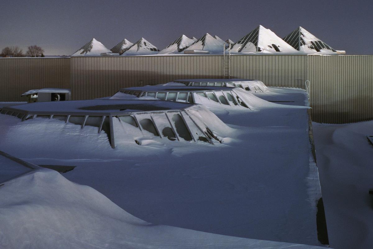 A snow-covered roof with multiple skylights and pyramid-shaped structures is visible under a dark sky.