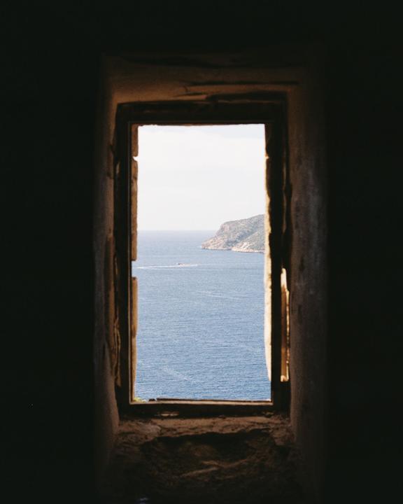 A view of the sea and a distant island is seen through a narrow window.