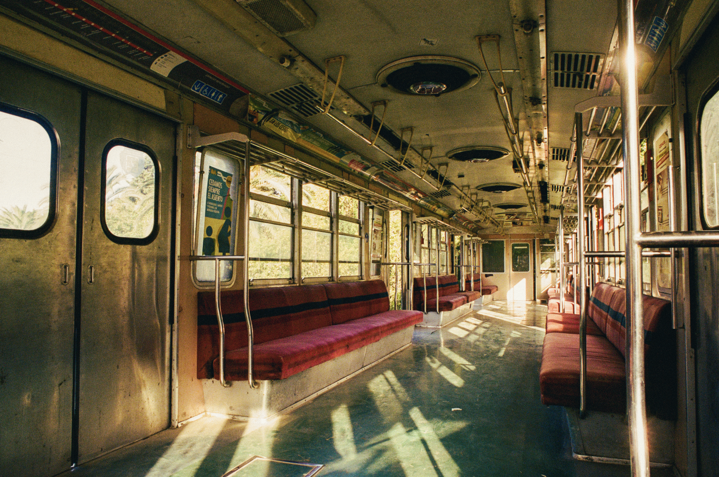 Sunlight streams through the windows of an empty train car with red seats.