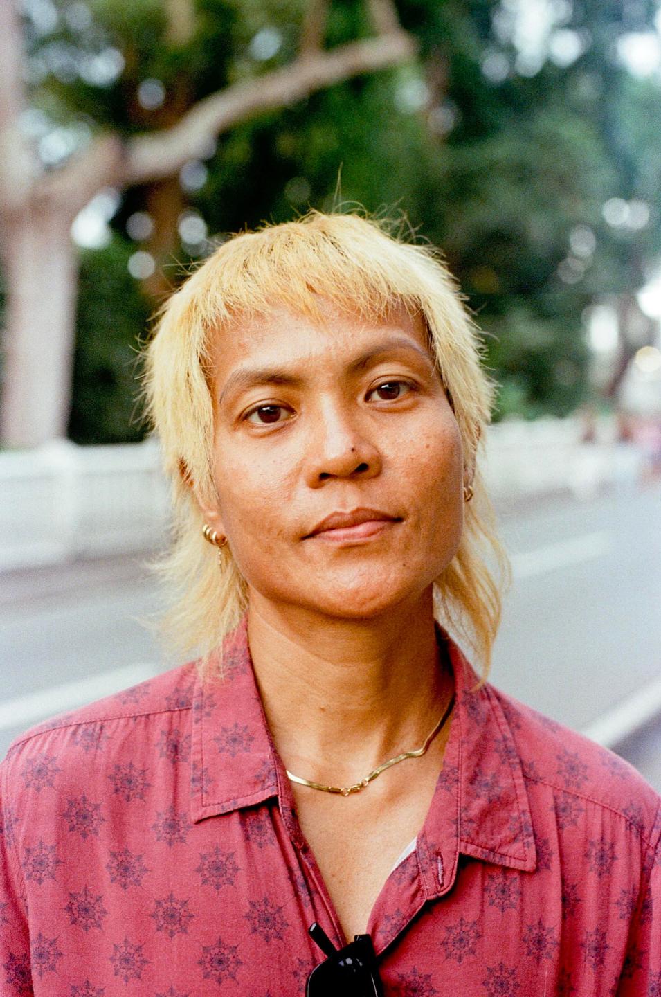 A woman with blonde hair and a red patterned shirt looks directly at the viewer.
