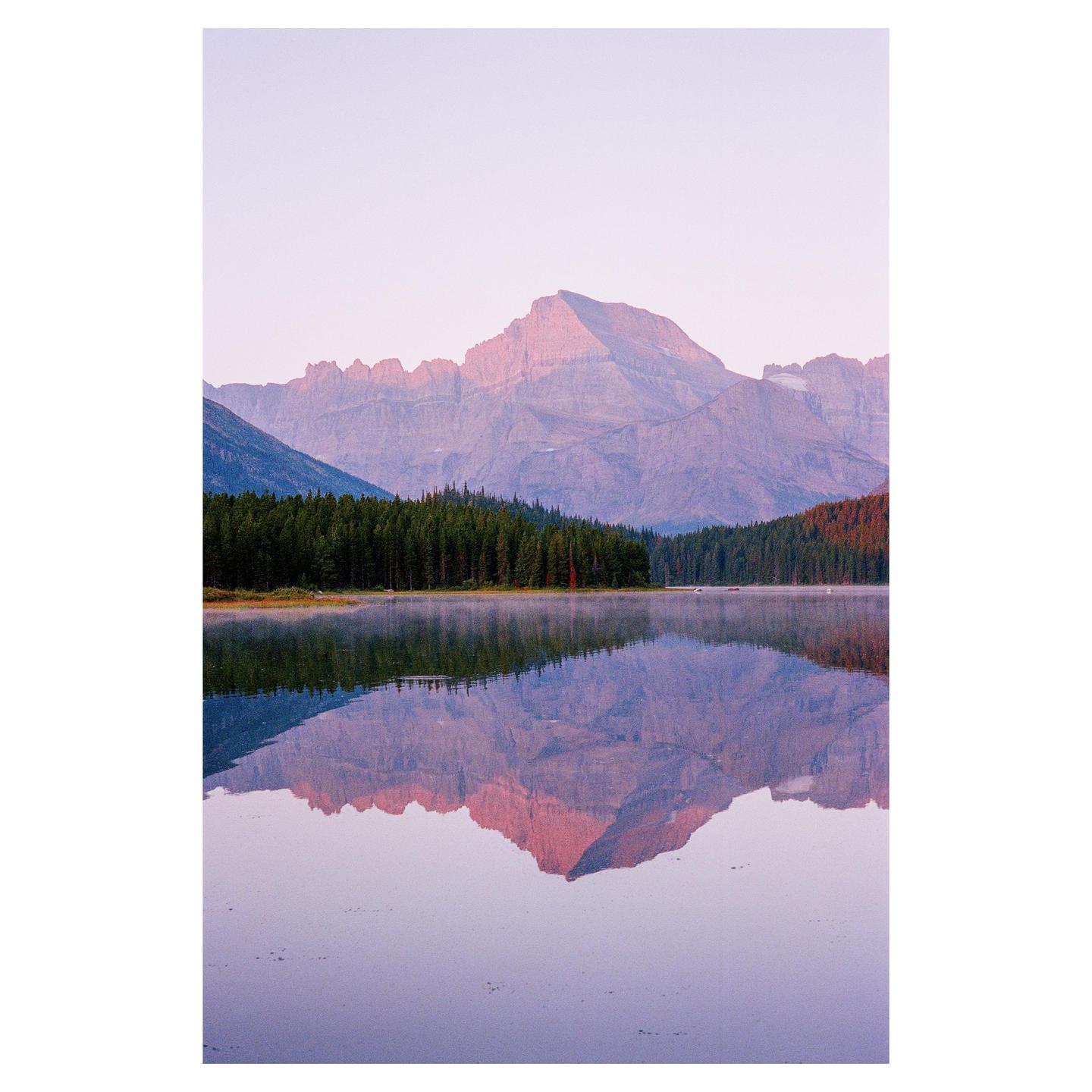 A mountain range with a forest at its base is reflected in a still lake.