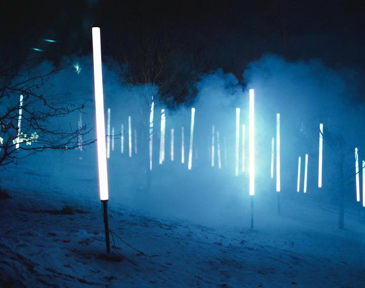 A snowy landscape at night is illuminated by many glowing light tubes and blue fog.