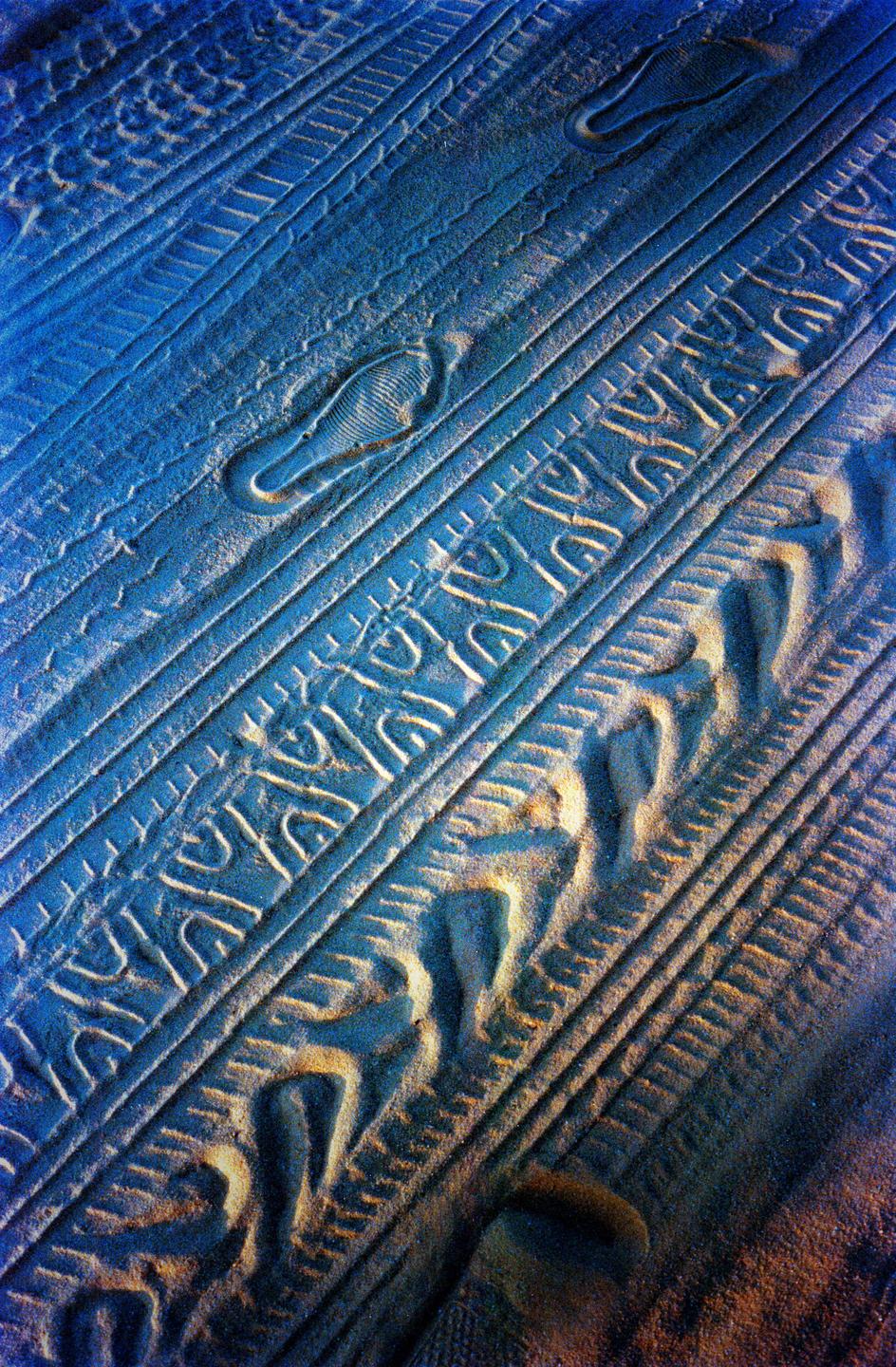 The blue sand shows various patterns and textures, including tire tracks and footprints.