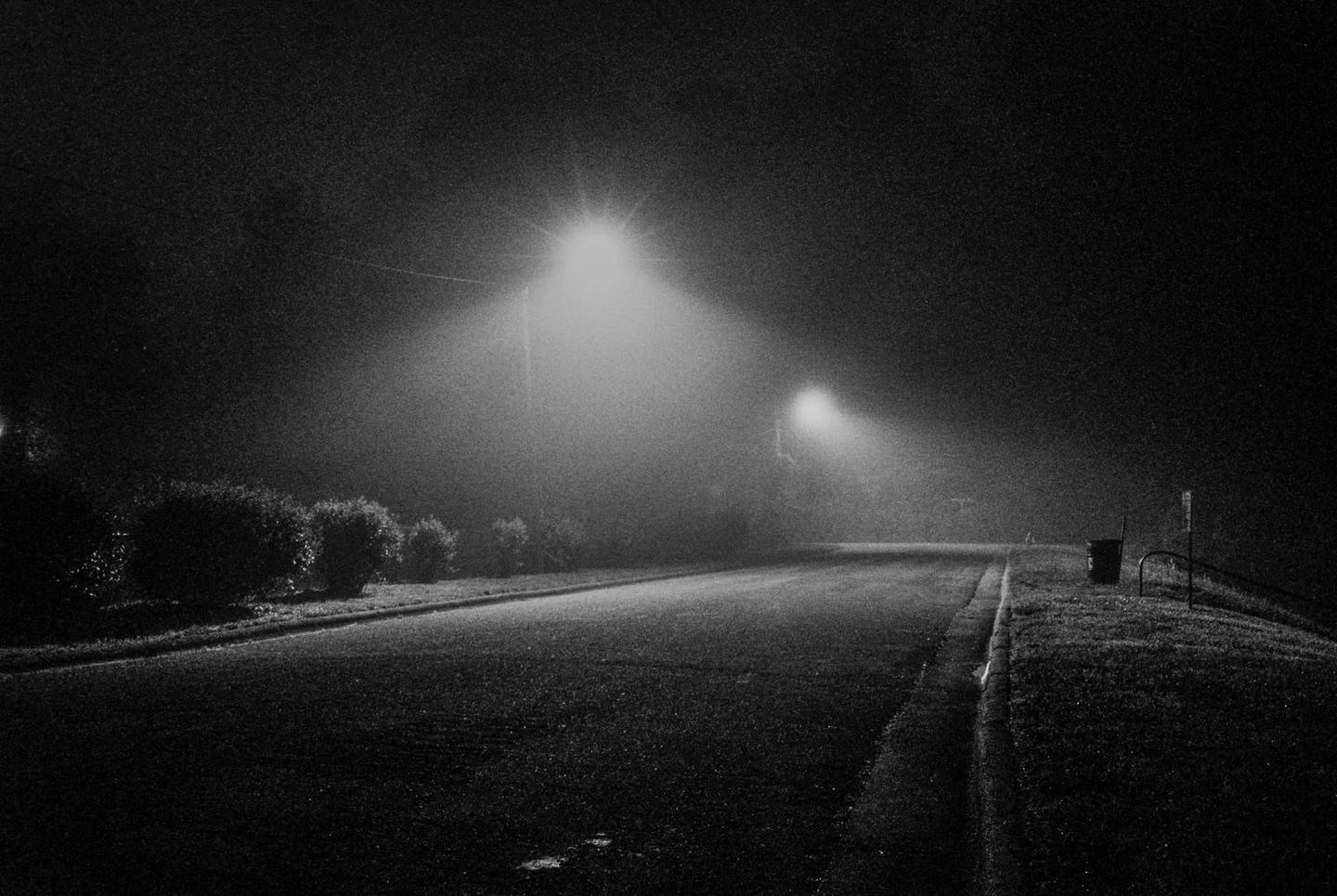 A street light illuminates a foggy road at night.