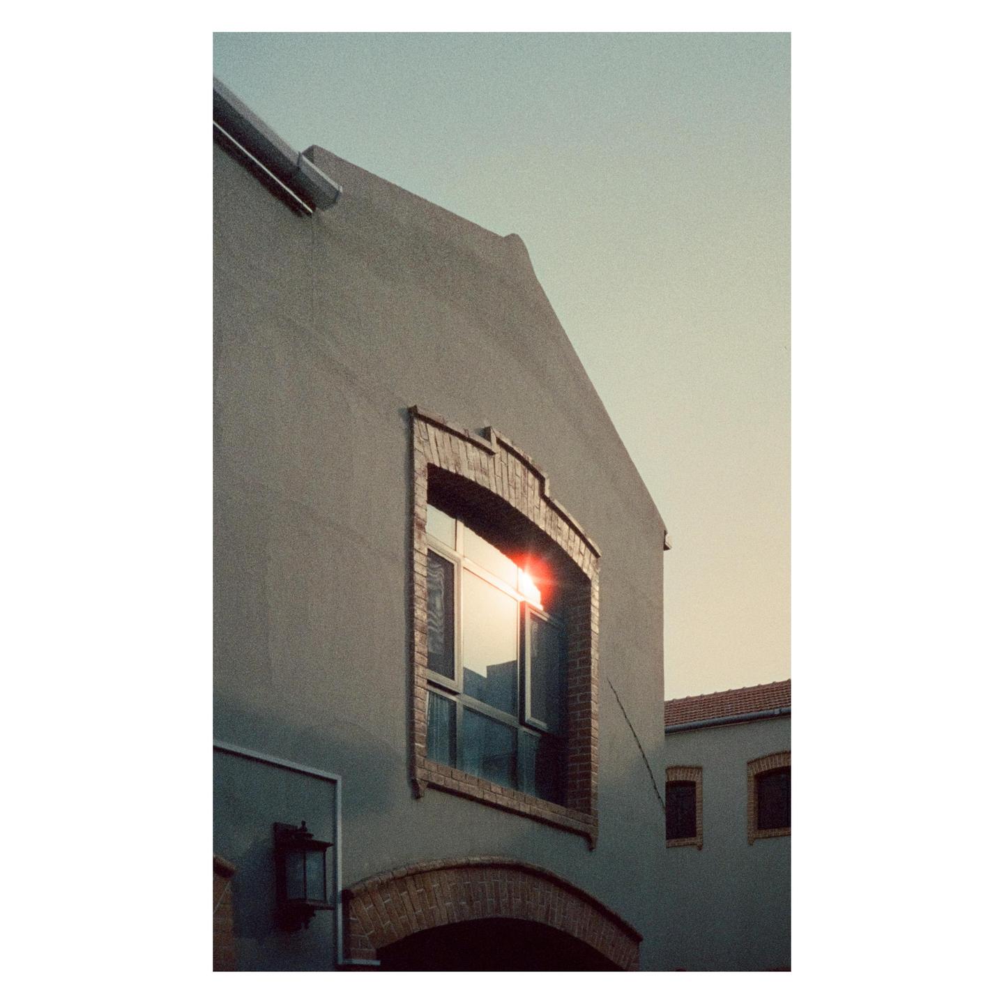 Sunlight reflects brightly off a window on a building with brick accents.
