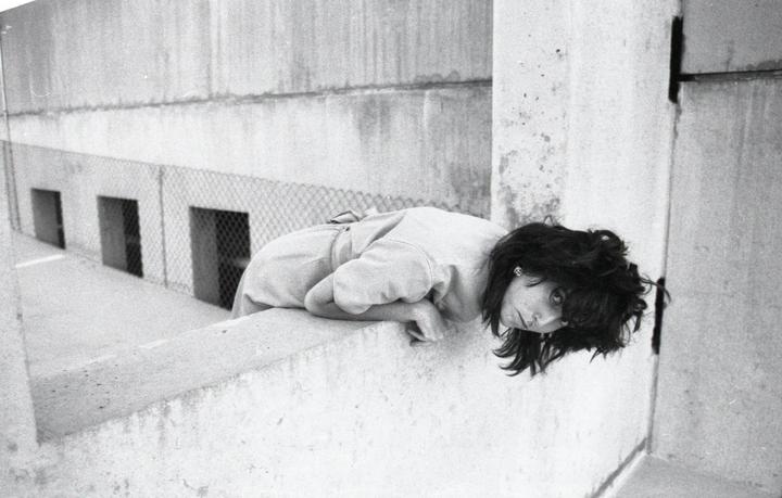 A woman leans over a concrete wall, looking up at the viewer.