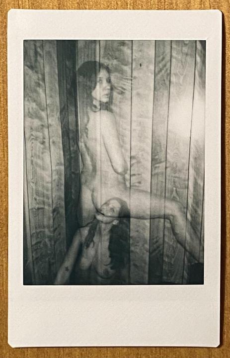 A double exposure shows a nude woman in two different poses against a wooden wall.