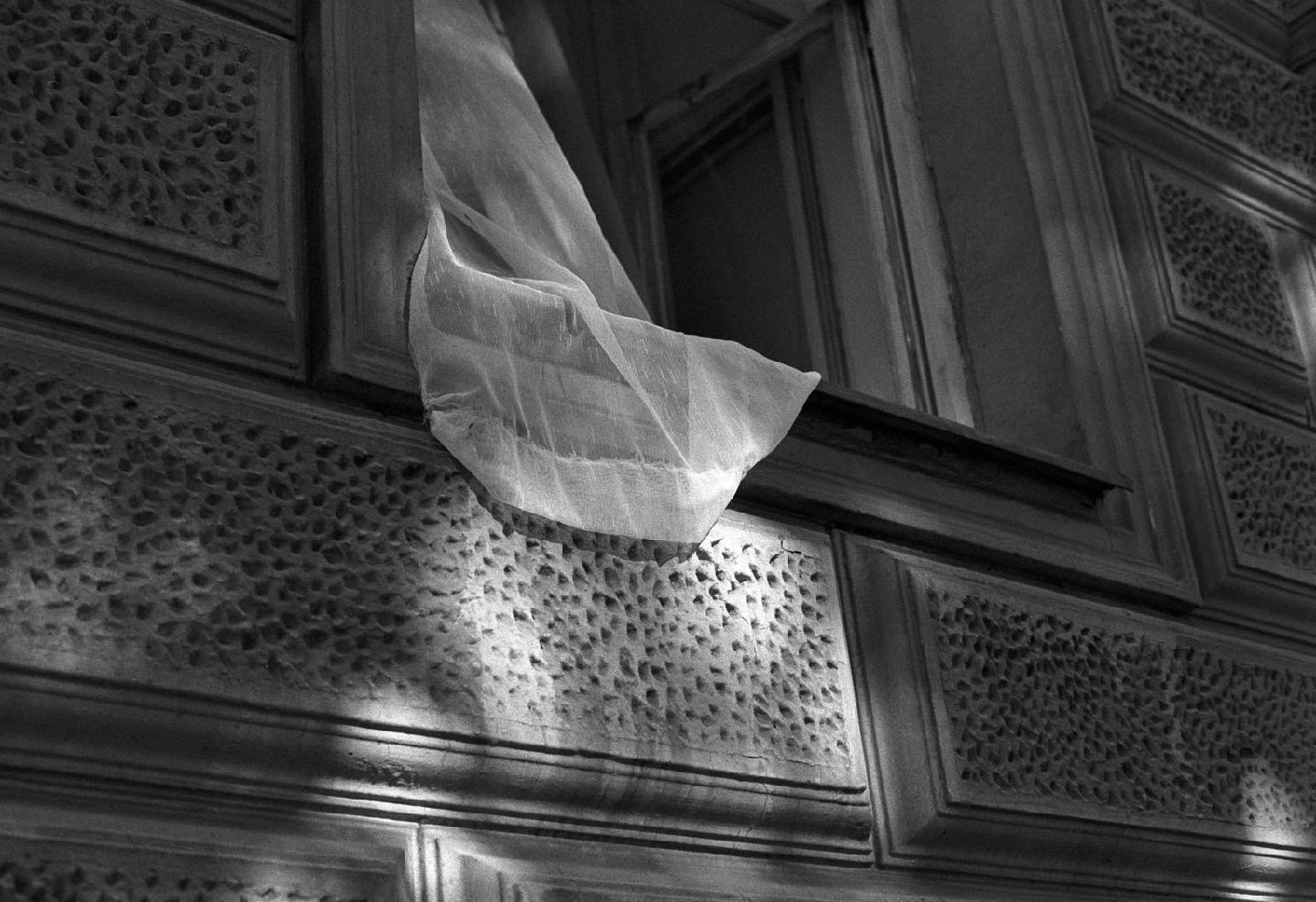 A sheer curtain billows out of an open window, casting shadows on a textured wall.