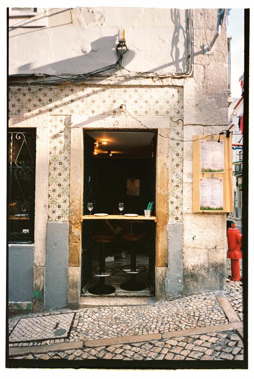 A small bar with two stools and wine glasses on a counter is visible from a cobblestone street.