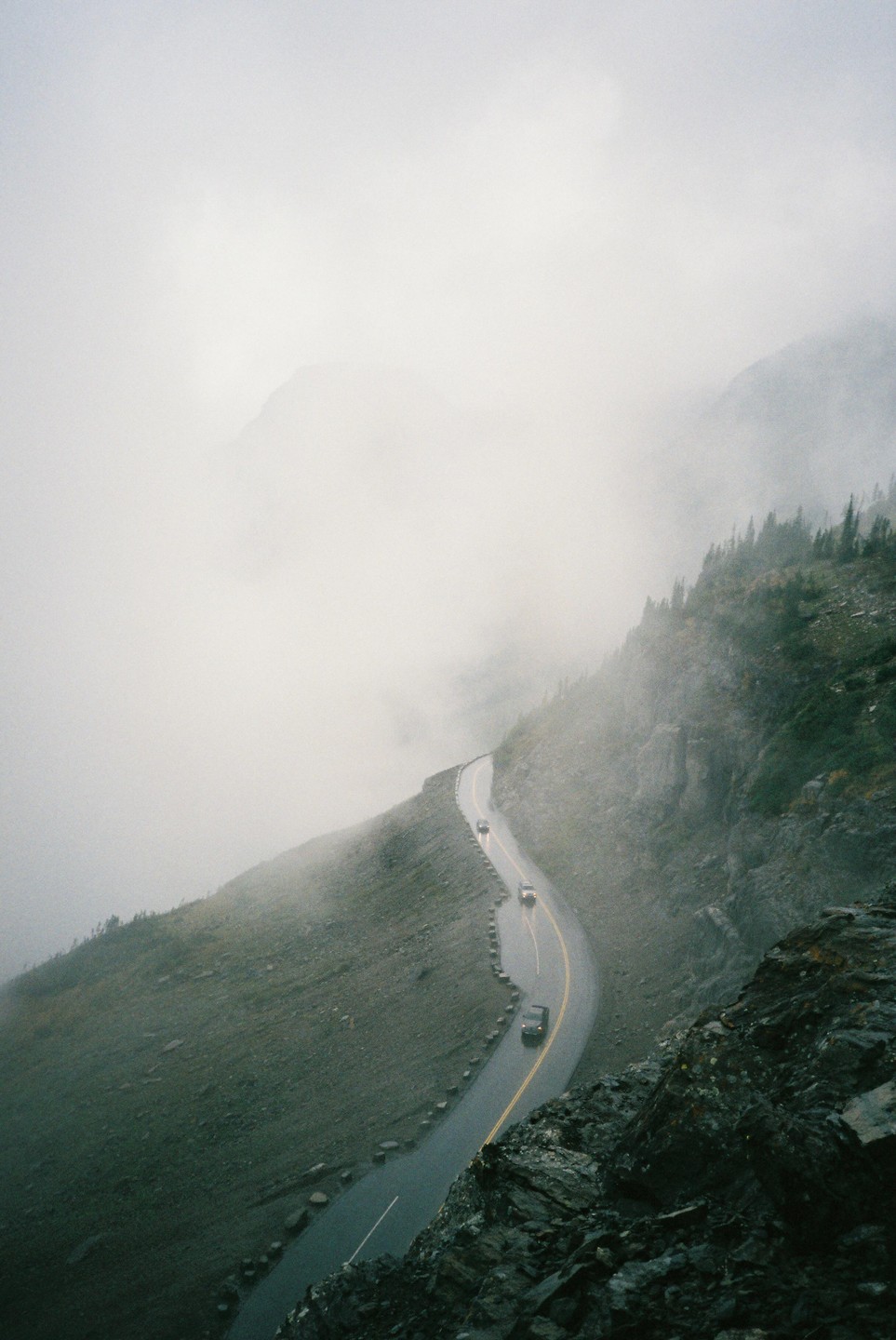 A winding road with cars on a mountain is shrouded in fog.