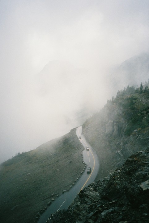 A winding road with cars on a mountain is shrouded in fog.