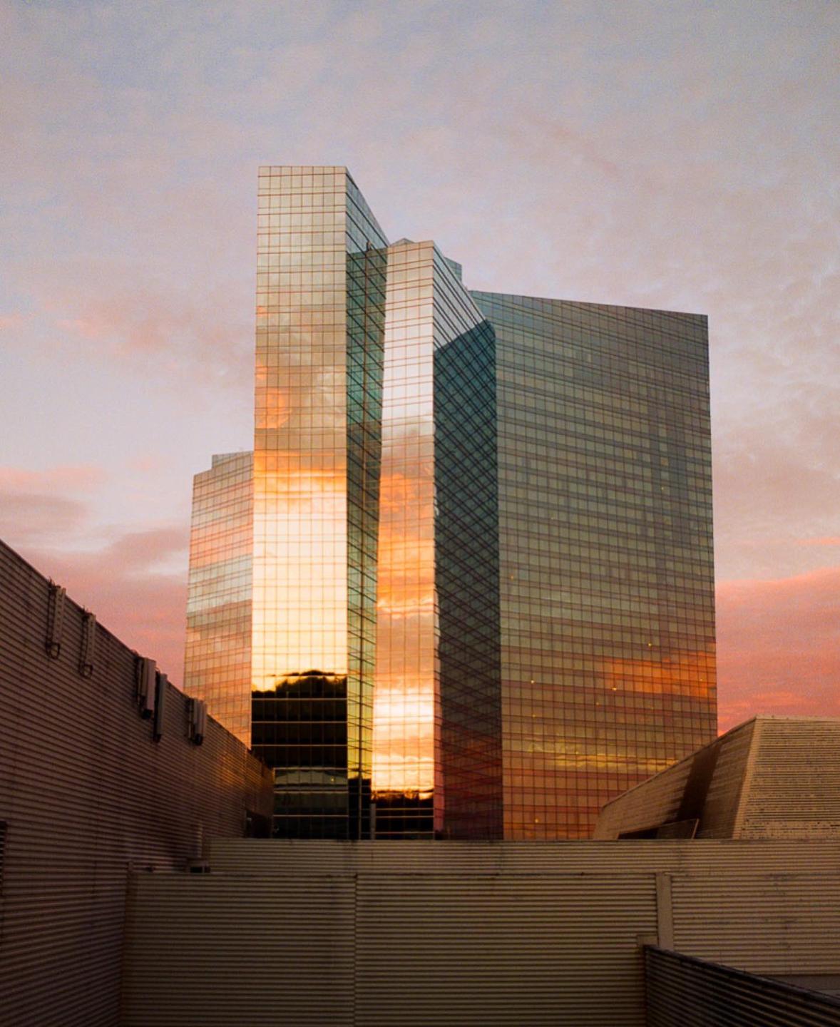 A glass skyscraper reflects a colorful sunset sky.